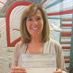 Photo of Marge holding donation check for Stein Hospice Camp Good Grief